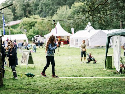 Mädchen auf Slackline an Bäumen vor Zelten